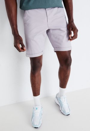 Lyse lavendel shorts med opfoldede manchetter, lavet af bomuldsstof, med forlommer, båret med hvide sneakers og hvide sokker. Enkel design, afslappet stil.