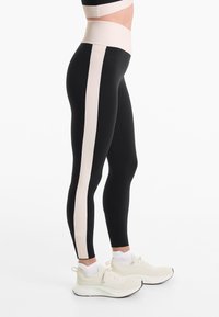 Magas derekú fekete leggings, széles világos bézs oldalsávval. Simább, rugalmas anyag. Bézs sportcipővel párosítva.
