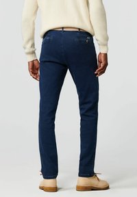Donkerblauwe denim broek met een slim fit. De achterkant heeft twee zakken en subtiele stiksels. Gekomplementeerd met beige schoenen voor contrast.