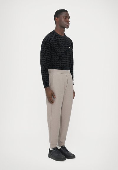 Μαύρο πουκάμισο με μακριά μανίκια που διαθέτει υφή με γεωμετρικό μοτίβο, σε συνδυασμό με ανοιχτό μπεζ παντελόνι στενής γραμμής και μαύρα αθλητικά παπούτσια.