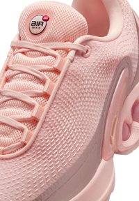 Zapatilla de malla rosa con parte superior texturizada, acentos suaves y una unidad de amortiguación de aire visible. Presenta cordones rosas y un logo en la lengüeta.