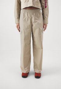 Beige cargo kalhoty s elastickým pasem, které mají dvě boční kapsy a rovný střih nohavic. Nosené s červenou obuví.