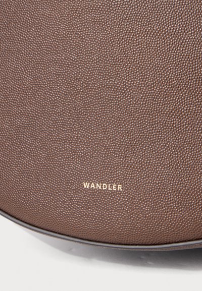 Gros plan d'un cuir marron texturé avec un motif finement grainé et le nom de marque WANDLER embossé en or près du bord inférieur.