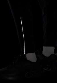Pantalons de sport noirs avec une bande réfléchissante blanche sur le côté, associés à des baskets noires et des chaussettes mi-mollet grises. La texture semble lisse.