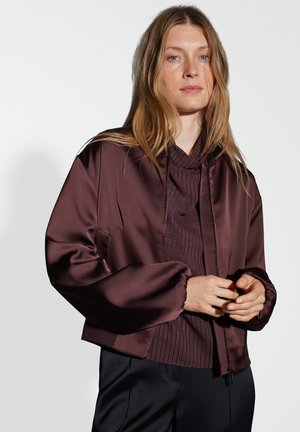 Burgunderrote Satin-Bomberjacke mit Reißverschluss vorne, gerippten Bündchen und lässiger Passform, die über einem strukturierten Strickoberteil getragen wird.