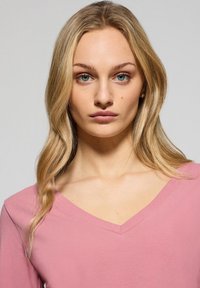 Ljust rosa V-ringad topp med långa ärmar, mjukt material och avslappnad passform. Kännetecknas av en enkel design och sömlös halsringning.