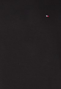 Camiseta de algodón negra con un pequeño logo bordado en rojo, blanco y azul en la parte superior izquierda del pecho. Diseño simple y sólido.