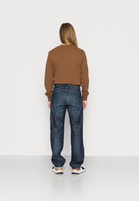 Brun långärmad tröja i kort modell; kombinerad med blå denimjeans med raka ben, utrustade med klassisk femficksdesign och subtila slitningsdetaljer.