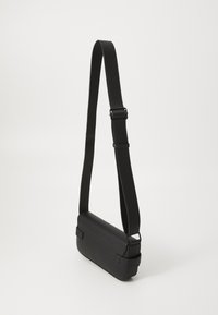 Borsa a spalla in pelle nera con una texture liscia, forma rettangolare e tracolla regolabile, caratterizzata da accessori semplici e un design minimalista.