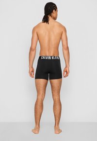 Crni pamukasti bokserice s širokim bijelim Calvin Klein pojasom, s prikazanom prilagođenom siluetom i glatkom teksturom iz zadnjeg pregleda.