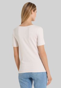 Korte mouwen, lichtroze top met een ronde halslijn en een gladde textuur, gecombineerd met lichtblauwe jeans, weergegeven van achteren.