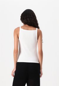 Camiseta sin mangas blanca de textura acanalada, con dobladillo recto y tirantes delgados. Llevada con pantalones negros de textura.
