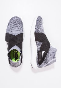Šedé a černé pletené slip-on tenisky Nike s bílými podrážkami a širokými černými elastickými pásky přes vrch. Jedna bota je ukázána z vrchu a druhá z boku.