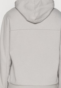 Haut à capuche gris clair en tissu doux, avec une capuche, sans logo visible, et un design simple et épuré sans embellissements.