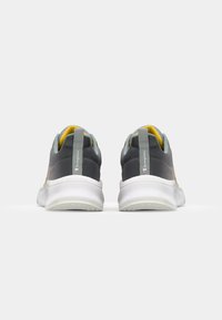 Grijze sportschoenen met gele accenten, ademend gaasstof, gevoerde kraag en witte rubberen zool, voorzien van een achterste treklip.