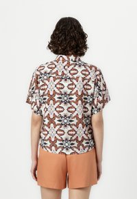 Short-sleeved patterned shirt with a floral design in shades of beige, brown, and navy, paired with orange shorts. Back view shown.