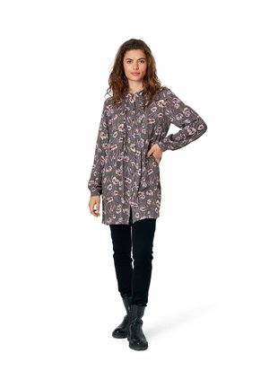 Floral patterned tunic in gray, featuring long sleeves, a buttoned front, and a relaxed fit. Paired with black pants and ankle boots.