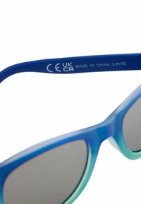 Occhiali da sole con gradiente blu e una montatura in plastica liscia, lenti grigie e una marcatura CE e UKCA sul braccio. Adatti per bambini di età compresa tra 3 e 6 anni.