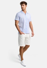 Lichtblauw overhemd met korte mouwen, verticale strepen, knoopsluiting aan de voorkant en een zachte textuur. Gecombineerd met witte shorts en witte sneakers.