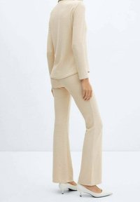 Ensemble haut en maille beige et pantalon évasé, avec une finition texturée. Le modèle porte des talons blancs et est vu de dos.