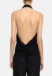 Czarny top na halter z głębokim dekoltem z tyłu, miękka tkanina, luźny krój i minimalne okucia. Posiada zwiewną sylwetkę w połączeniu z przejrzystymi spodniami.