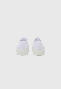 White lace sneakers with rubber soles, featuring a textured lace pattern on the upper part and a solid white heel cap.