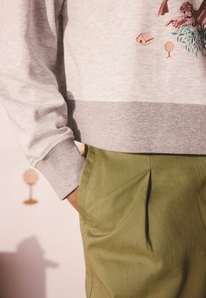 Siva jopica z rebrastim robom in žepom, okrašena s pisanimi vzorci živali in hiš. Olivno zelene hlače z gubami in stranskimi žepi.