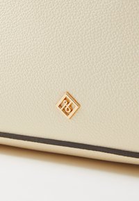 Surface en cuir beige texturé avec un petit emblème carré doré présentant un logo stylisé "RS" près du bord inférieur.