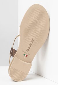 Suola color tan di un sandalo con un motivo testurizzato, caratterizzato da un cinturino in bronzo metallico e dal nome del marchio in rilievo "NeroGiardini," contrassegnato "Made in Italy."