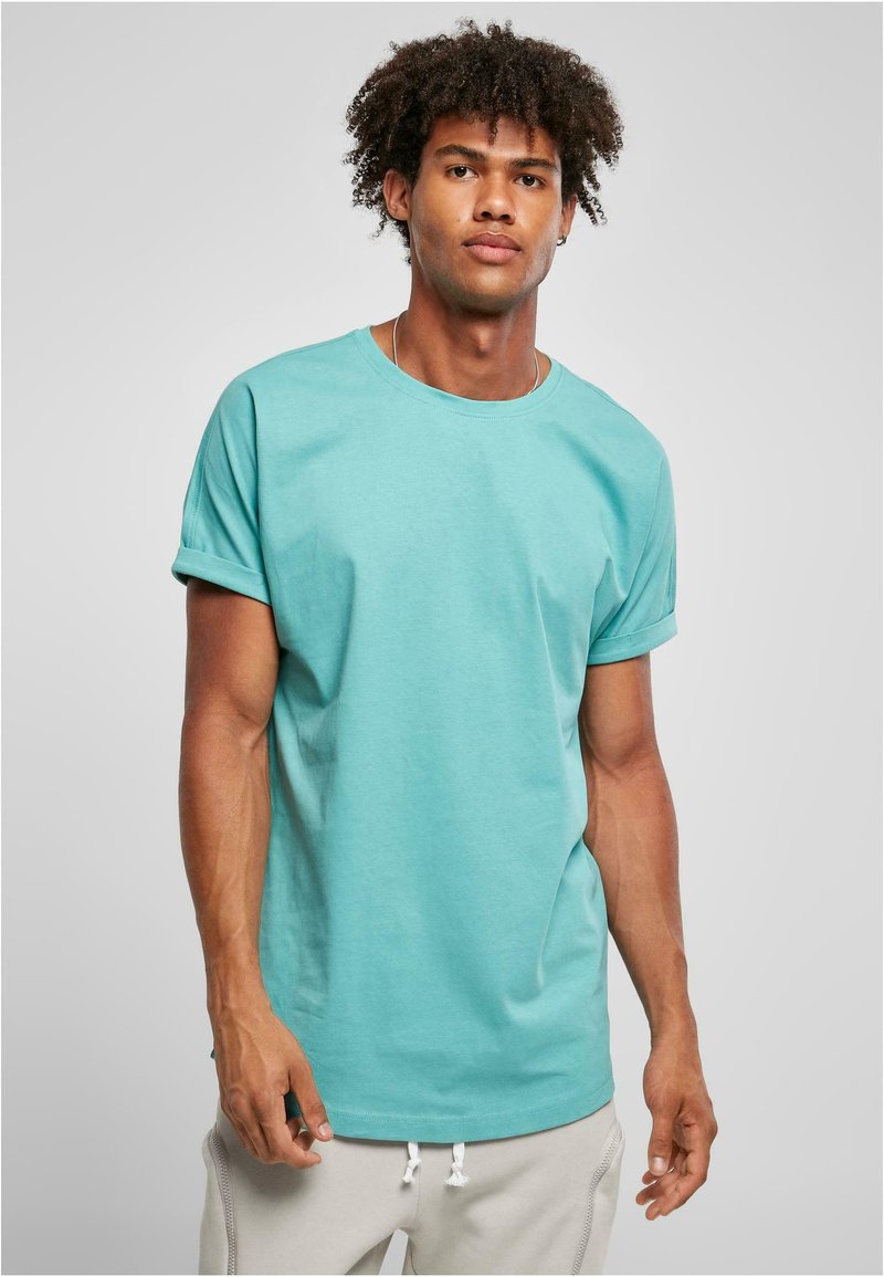 Camiseta de cuello redondo color turquesa en algodón suave con mangas cortas enrolladas, combinada con pantalones de chándal gris claro con detalle de cordón.