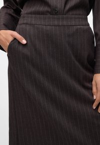 Close-up of person wearing dark pinstripe skirt and matching top with hand in skirt pocket.