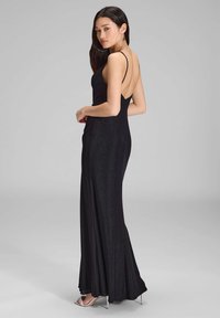 Mustapuku, jossa on siisti, kapea siluetti, selkä auki -suunnittelu ja kiiltävä pinta, ohut hihna ja levenevä helma.