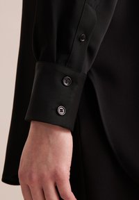 Schwarzer Langarmhemd-Manschette mit zwei schwarzen Knöpfen, ausgestattet mit einer glatten Stoffstruktur und einem maßgeschneiderten Design.