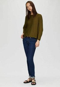 Olijfgroene gebreide trui met lange mouwen, gecombineerd met donkerblauwe skinny jeans en zwarte sandalen met bandjes. Eenvoudige en casual outfit.