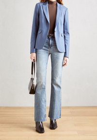 Ljusblå blazer med slag, kombinerad med högmidjade ljusblå marängbyxor. Modellen håller en liten svart handväska och har på sig ankelstövlar.