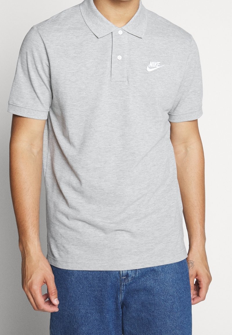 Grå bomullspolo med krage och korta ärmar, med en vit Nike-logotyp på vänster bröst. Enkel, klassisk design.