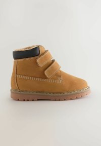 Beige Knöchelstiefel aus Wildleder mit einem weichen Futter, schwarzen Akzenten oben, doppelten Klettverschlüssen und einer strukturierten Gummisohle.