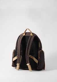 Rucsac maro cu model, cu bretele din plasă neagră căptușite, accesorii aurii și buzunar lateral cu fermoar. Dispune de o mână de prindere pentru transport.