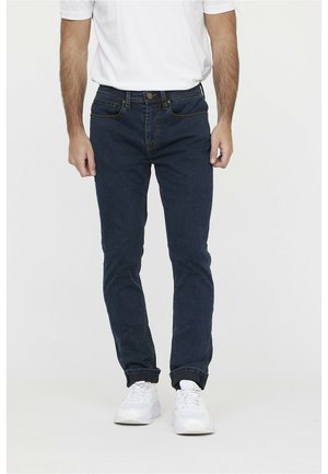 Donkerblauwe jeans met een slim fit, voorzien van voorzakken, lichte stiksels en een knoopsluiting, gecombineerd met witte sneakers.