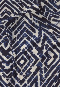 Tessuto a maniche corte caratterizzato da un motivo geometrico blu e bianco, con texture stratificate e forme varie, realizzato in un materiale leggero.