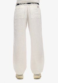 Witte linnen broek met wijde pijpen, een zwarte merkband en twee achterzakken, gemaakt van een lichte, gestructureerde stof.
