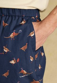 Jūras spēku šorti ar nerimstošu putnu apdruku dažādās pozās un aktivitātēs, ar elastīgu jostasvietu un sānu kabatu detalizāciju.