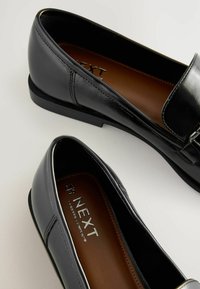 Paire de mocassins en cuir noir à enfiler avec petits talons, semelles intérieures marron estampillées «NEXT Forever Comfort», présentée sur fond blanc.