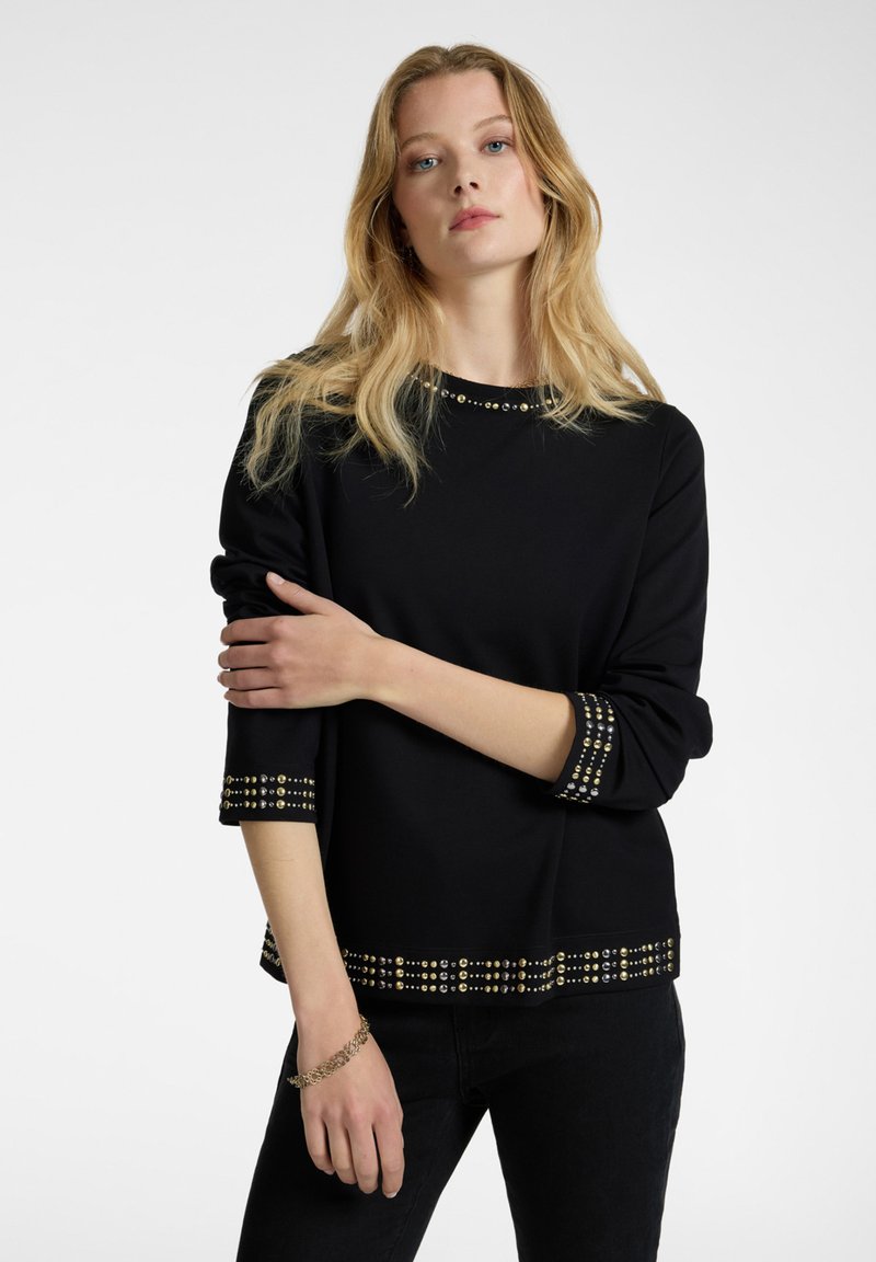 Sudadera negra con adornos en el cuello y las mangas, que presenta un corte relajado y mangas de tres cuartos.