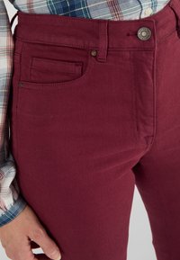 Pantalones burdeos de corte ajustado, con un bolsillo frontal y botón de metal, fabricados en una suave mezcla de algodón con una textura lisa.