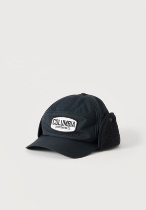 Czarna czapka Columbia Sportswear z nausznikami, naszywką z logo na przodzie i zakrzywionym daszkiem na jasnym tle.
