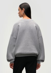 Felpa grigia oversize con spalle cadenti e polsini a costine, realizzata in tessuto morbido, dotata di scollatura rotonda e senza motivi in evidenza.