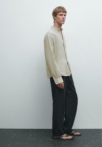 Beige linned knap-op skjorte, mørke løse bukser og sorte flip-flops. Simpelt design med minimal accentuerings, struktureret stof.