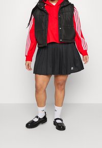 Czarna ocieplana kamizelka na czerwonym hoodie w białe paski, w połączeniu z czarną plisowan�ą spódnicą i czarnymi butami. Dodatki to białe skarpetki.