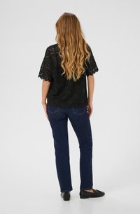 Svart spetsblus med vida ärmar och vågig nederkant, ihop med mörkblå raka jeans och svarta lägenheter, sedd bakifrån.